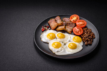 Delicious nutritious breakfast of fried quail eggs, bacon, legumes and cherry tomatoes