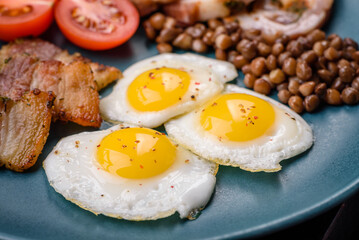 Delicious nutritious breakfast of fried quail eggs, bacon, legumes and cherry tomatoes