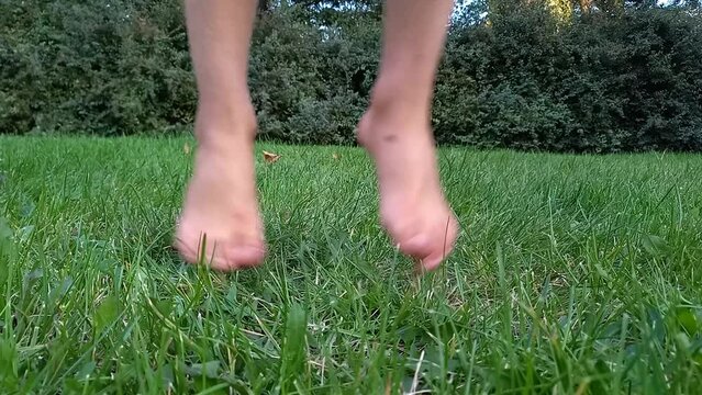 Happy child jumping on green grass in park barefoot. close-up legs of boy walking barefoot on lawn in summer. Happy childhood. Hardening, active healthy lifestyle. Bottom view
