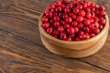red hawthorn berries in wooden bowl on flat wooden surface.