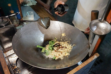 A man cooking fried noodles on steel skillet pan for selling on the street food. Indonesian call the dish Bakmie Goreng. Indonesian Street food culinary