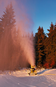 Snowmaker producing snow in a ski resort. Snowjet in side light and with dark background at sunset