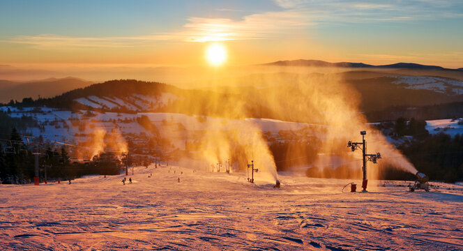 Ski slope in winter resort with skiers and snow making guns at sunset, Slovakia