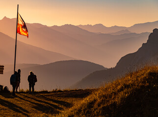 Alpine summer sunrise with a flag and unknown hiker silhouettes at Mount Kreuzjoch, Fulpmes,...