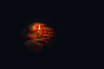 Candle in the hands.Man hands holding a burning candle on dark background.Religious concept.Copy...