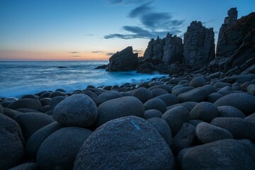 Beach shore with large rocks and crashing waves illuminated by the warm glow of the sunset sky