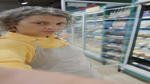 Vertical handheld POV of Caucasian female shop assistant showing readymade food in fridges at camera while recording video blog from workplace