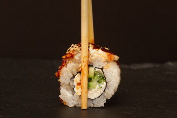 Sushi roll with eel and cheese with chopsticks on a dark background.