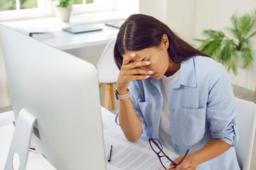 Stressed, tired, sad, depressed, overworked woman sitting at her office desk with computer, holding...