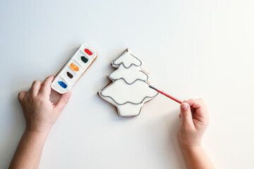 A child paints a gingerbread in the shape of a Christmas tree, an idea for creativity with children