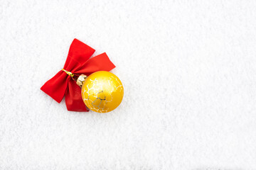 Gold Christmas decoration bauble with red ribbon bow isolated on white snow background.