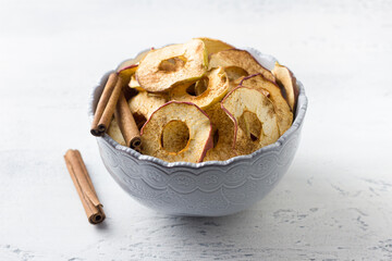 Homemade dried apples with cinnamon, apple chips in a bowl with cinnamon sticks on a light gray background. Delicious healthy snack