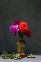 Still life with flowers. Pink, red dahlias in a dark vase, pink fabric, small pink cup, dark background