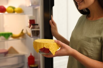 Woman holding bowl of fresh tomatoes covered with beeswax food wrap in kitchen, closeup