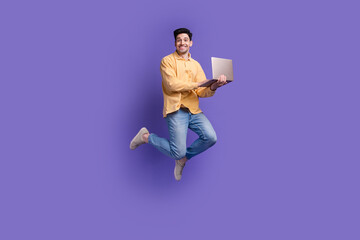 Full body photo of nice young male jump hold netbook ecommerce wear trendy yellow outfit isolated on violet color background
