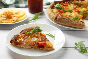 Plate with piece of delicious pineapple pizza on white wooden table