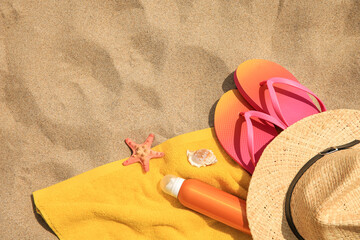 Fototapeta na wymiar Straw hat, flip flops and other beach items on sand, flat lay. Space for text