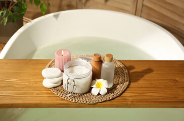 Wooden tray with spa products, stones and burning candle on bath tub in bathroom
