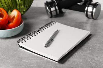 Healthy diet. Vegetables, dumbbells, notebook and pen on grey table