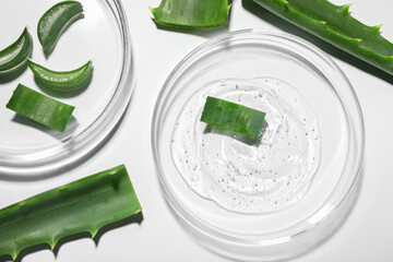 Petri dishes with cosmetic gel and cut aloe vera on white background, flat lay