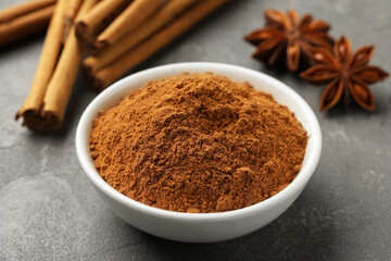 Bowl of cinnamon powder, sticks and star anise on grey table, closeup