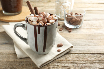 Delicious hot chocolate with marshmallows and cocoa powder in cup on wooden table, space for text