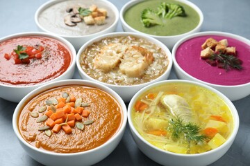 Tasty broth and different cream soups in bowls on gray table, closeup