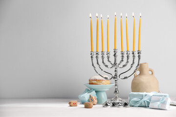 Hanukkah celebration. Menorah with burning candles, dreidels and gift boxes on white table, space...