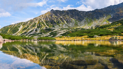 Fototapeta na wymiar Polish Tatra Mountains, natural lake Przedni Staw Polski surrounded by high mountain peaks, view from the mountain hiking trail on a sunny summer day.