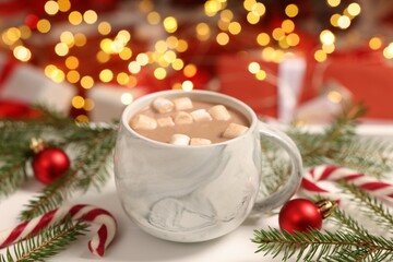 Delicious cocoa with marshmallows, Christmas decor and candy cane on table against blurred lights, closeup