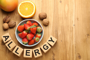 Food allergy. Walnuts, strawberries, citrus fruits and cubes on wooden table, flat lay with space for text
