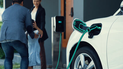 Modern family with young girl recharge electric car, EV charger from home charging station plugged...