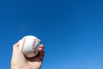 青空と野球のボールを握る男の手（30代、日本人）