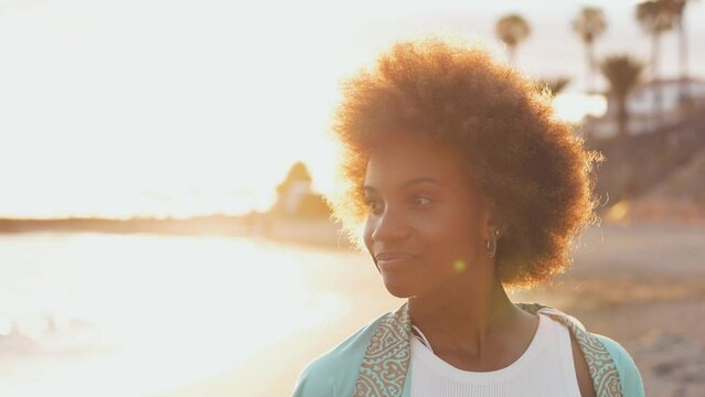 One young beautiful afro woman walking on the sand of the beach enjoying summer and having fun outdoors with sunset in the background. People vacations free time concept enjoy
