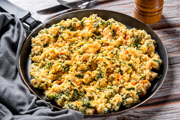 scrambled eggs with spinach and tomato in pan on wooden table background - obrazy, fototapety, plakaty