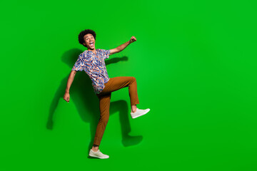 Full length photo of positive cheerful man dressed print shirt walking empty space isolated green color background