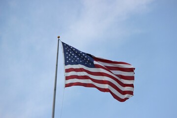 Vibrant American flag of red, white, and blue colors, waves in the wind against a clear blue sky