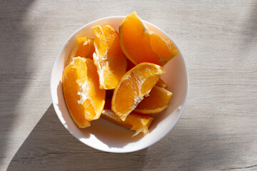 Picture of juicy fresh orange wedges in a bowl. Healthy snack on the kitchen table. Beautiful bright sunlight. Top view of summer fruit