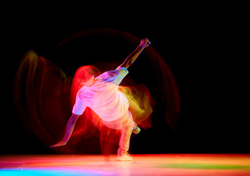 Dance show. Athletic guy dancing contemp, breakdance and hip-hop against black studio background in mixed neon light with motion blur.