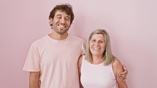 Joyful mother and son grinning toothily, exuding happiness and confidence while standing together over an isolated pink background