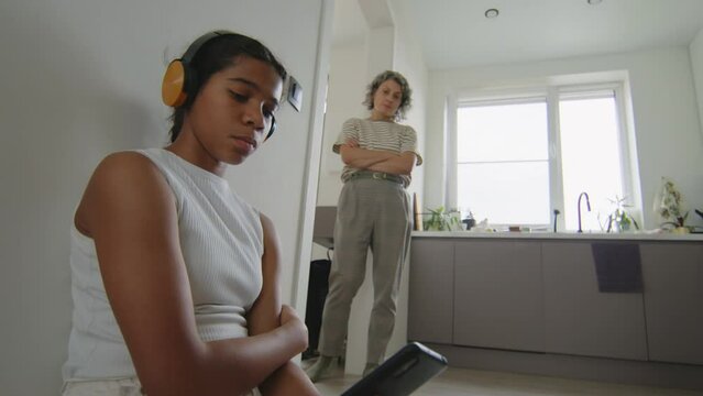 Mother looking at her sad daughter listening to music in headphones