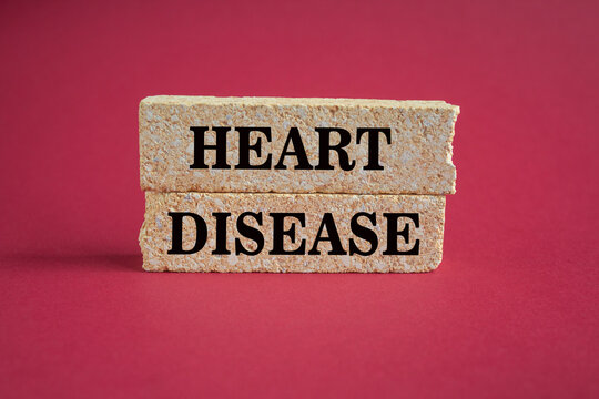 Medicine and health symbol. Concept words HEART DISEASE on brick blocks. Beautiful red background. Businessman hand. Medical and heart disease concept. Copy space.