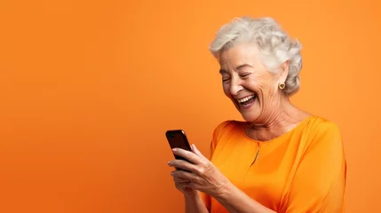 Fototapeten Happy senior woman waving on video call through smart phone against orange background © Olga