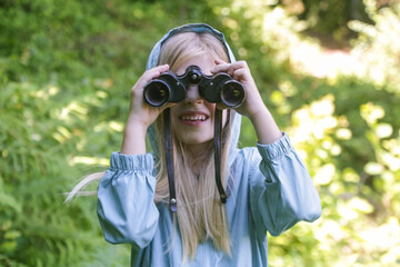 Cute little girl exploring nature looking through binoculars. Child playing outdoors. Kids travel, adventure and bird watching concept.	