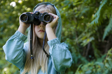 Cute little girl exploring nature looking through binoculars. Child playing outdoors. Kids travel,...