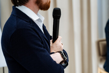 Business coach holding microphone in hand, speaker speech at seminar, guy in suit speaking into...