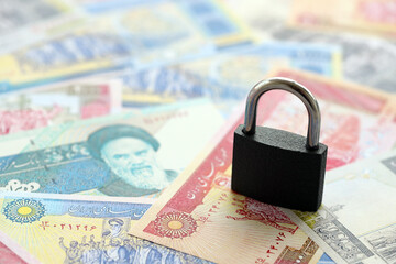 Small padlock lies on pile of iranian money close up. Sanctions, ban or embargo concept - obrazy, fototapety, plakaty