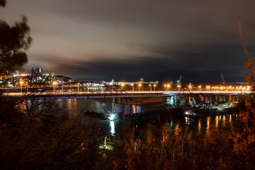 Foto op Plexiglas Night photo of a road bridge over a river, a cityscape. Lanterns of the night city. © Aleksey