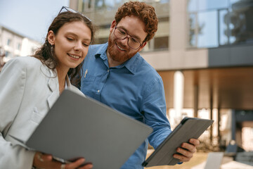Smiling business colleagues discuss biz issue while use laptop standing on building background