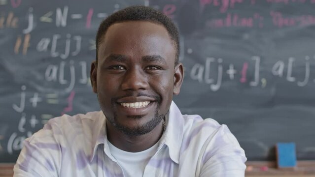 Portrait of young joyous African American student smiling on camera while sitting in college classroom during programming lesson